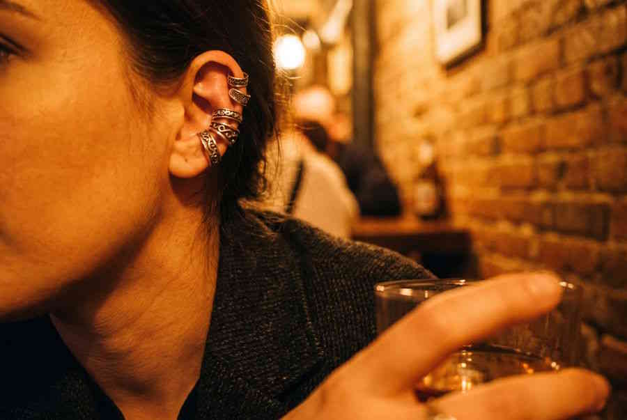 Fake Ear Cuffs – Frau mit mehreren silbernen Ear Cuffs am Ohr in Bar-Atmosphäre