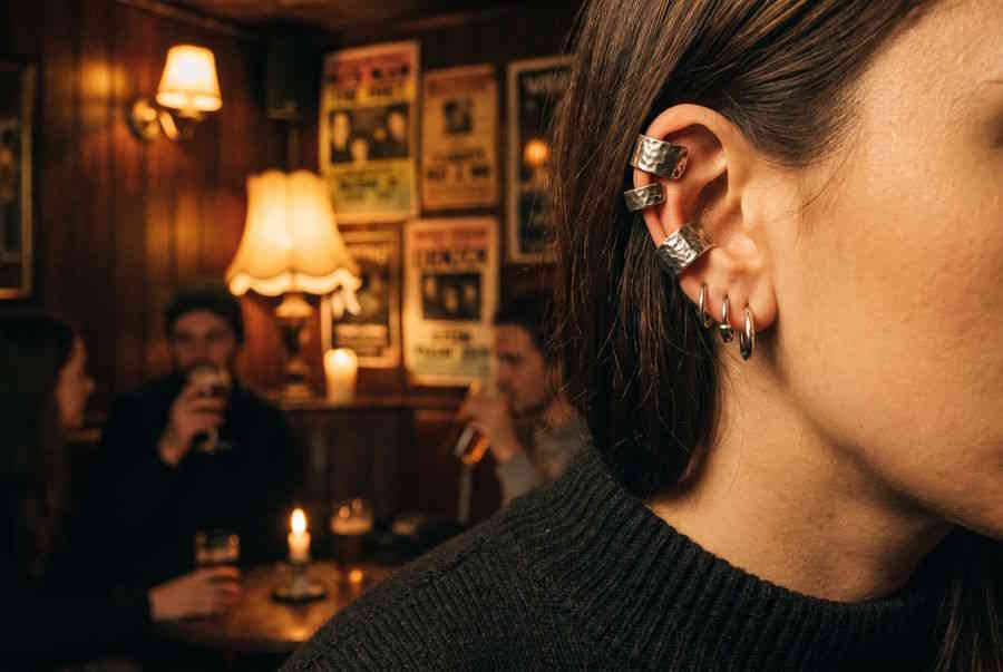 Ear Cuffs – Frau mit mehreren silbernen Ear Cuffs am Ohr in Bar-Atmosphäre