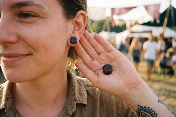 Gedehntes Ohr mit dunkelbraunem Holz Plug und zusätzlichem Plug als Größenvergleich in der Hand
